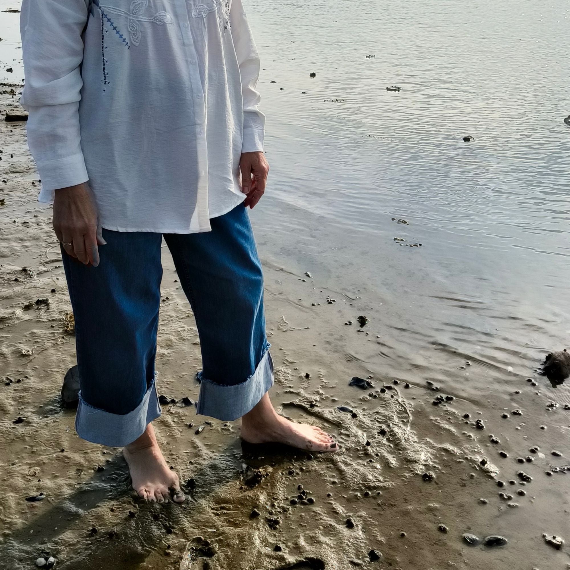 Cropped denim bukser med OEKO-TEX® bomuld og opsmøg/opslag – Helle  med fokus på den hvide skjorte med broderi og de cropped denim bukser ved Roskilde fjord i Frederikssund - Et Sanset Univers