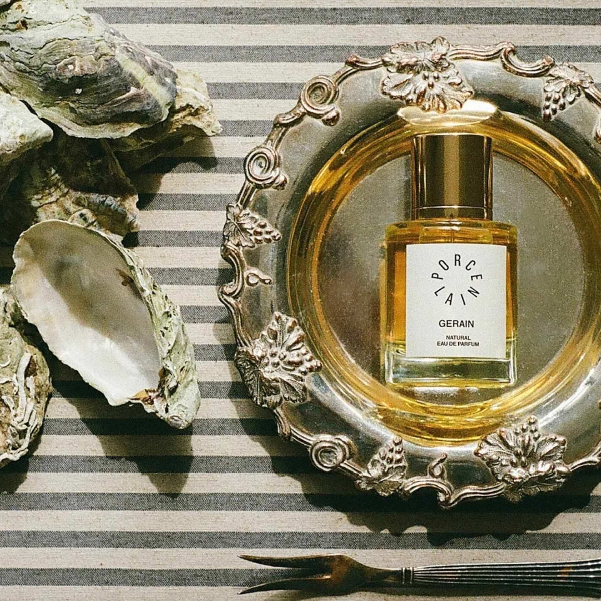 PORCELAIN Gerain No. 5 – naturlig parfume stylet på sølvfad med stribet dug, østers og østersgaffel – Et Sanset Univers