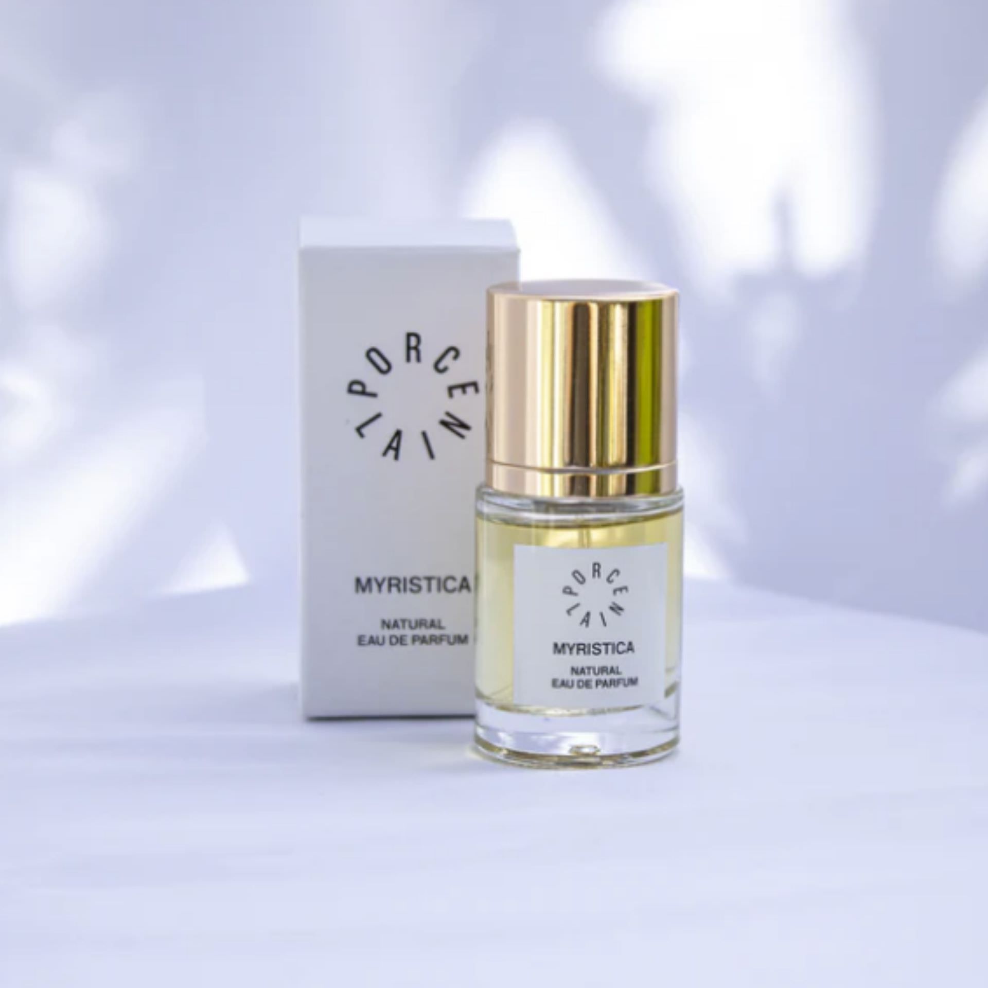 PORCELAIN Myristica No. 2 – naturlig parfume stylet på hvid dug med skyggespil fra grønne grene – Et Sanset Univers